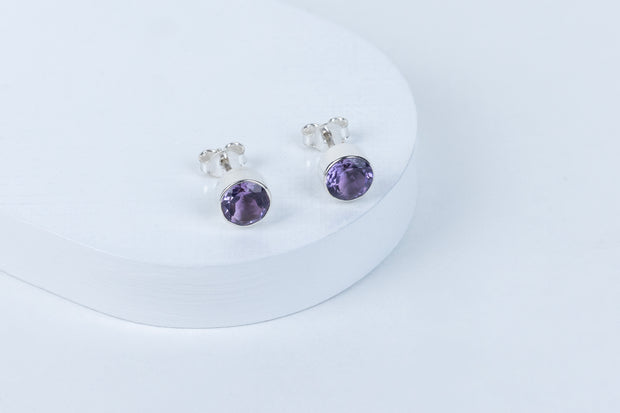 A pair of purple amethyst stud earrings on a white surface.