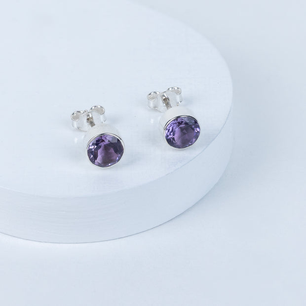 A pair of purple amethyst stud earrings on a white surface.