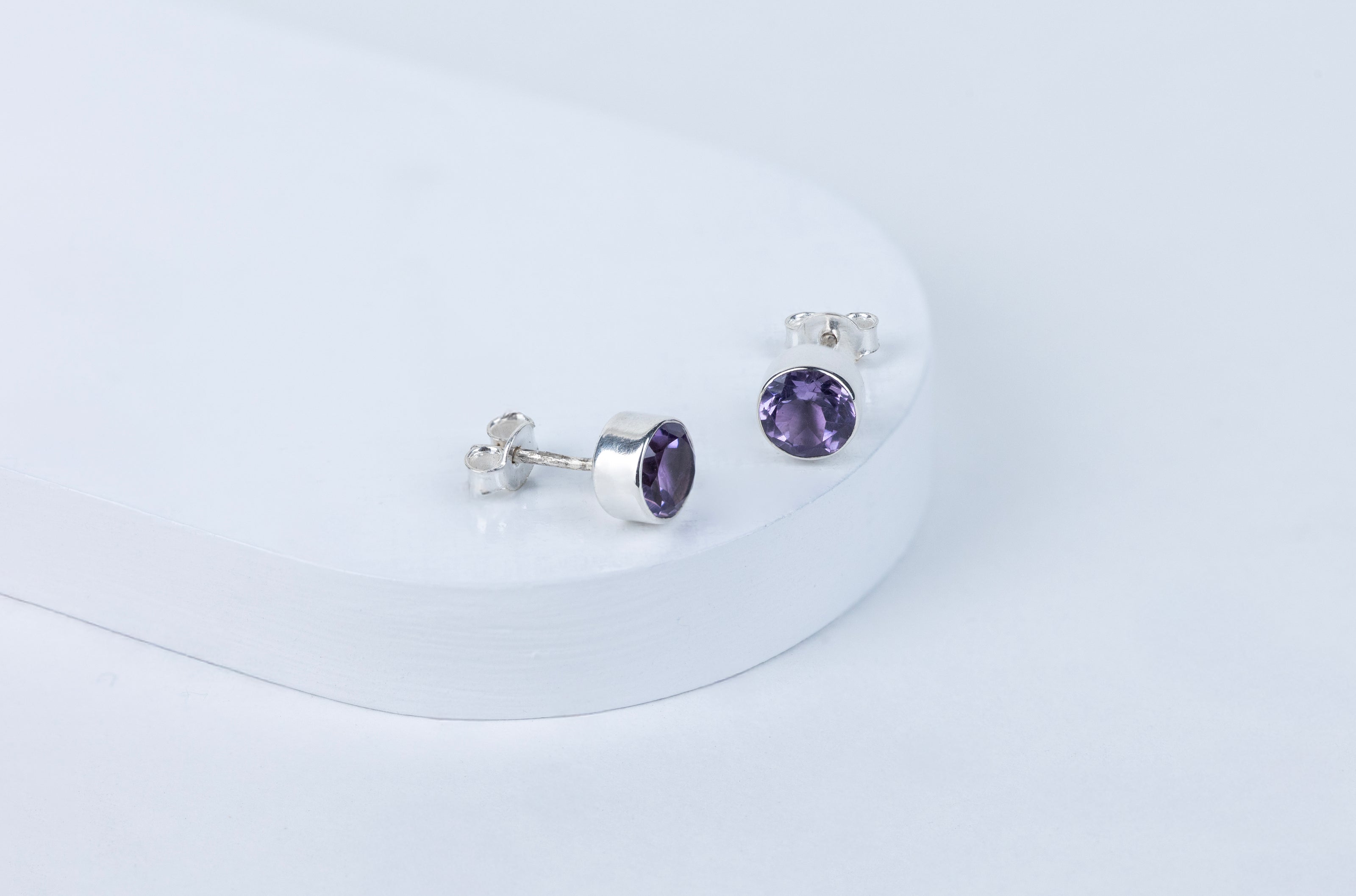Pair of silver earrings with purple gemstones on a white background