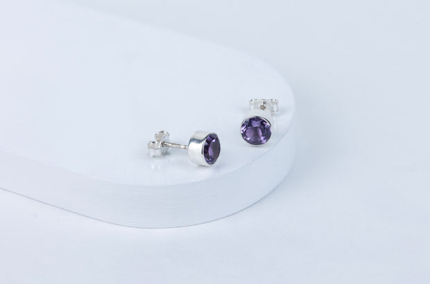 Pair of silver earrings with purple gemstones on a white background