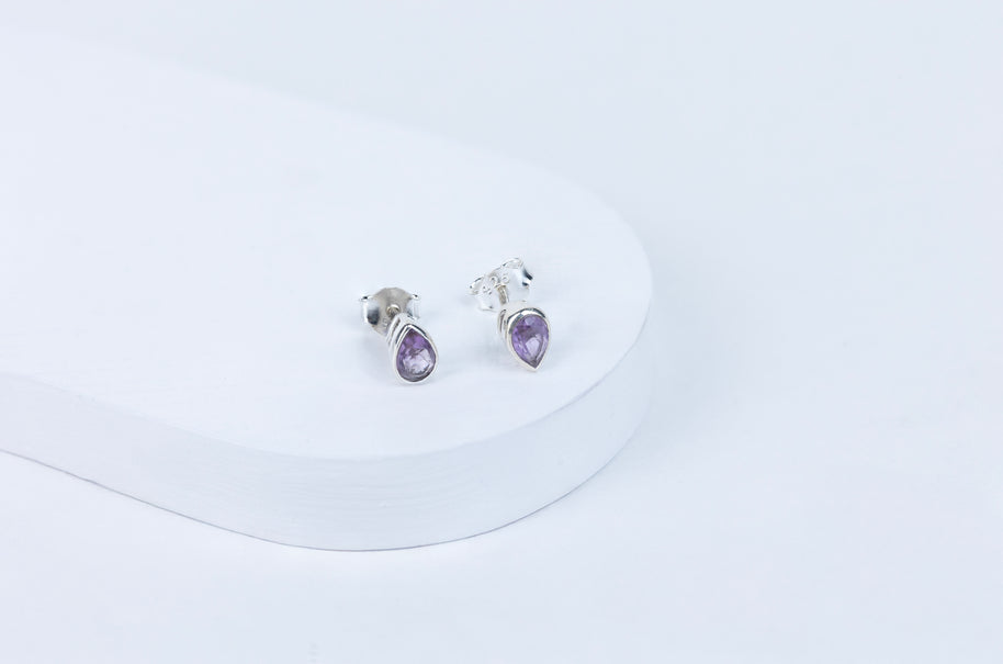 A pair of amethyst oval earrings set in silver mounting, displayed against a white background.