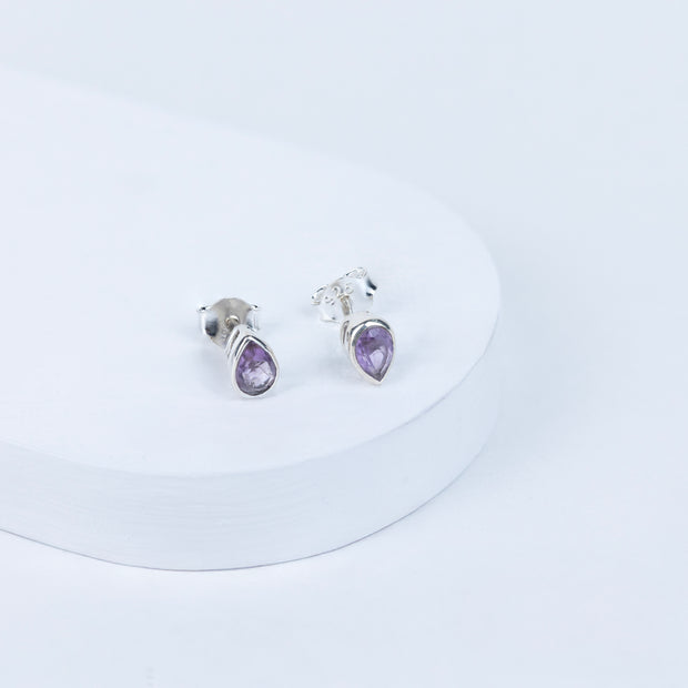 A pair of amethyst oval earrings set in silver mounting, displayed against a white background.