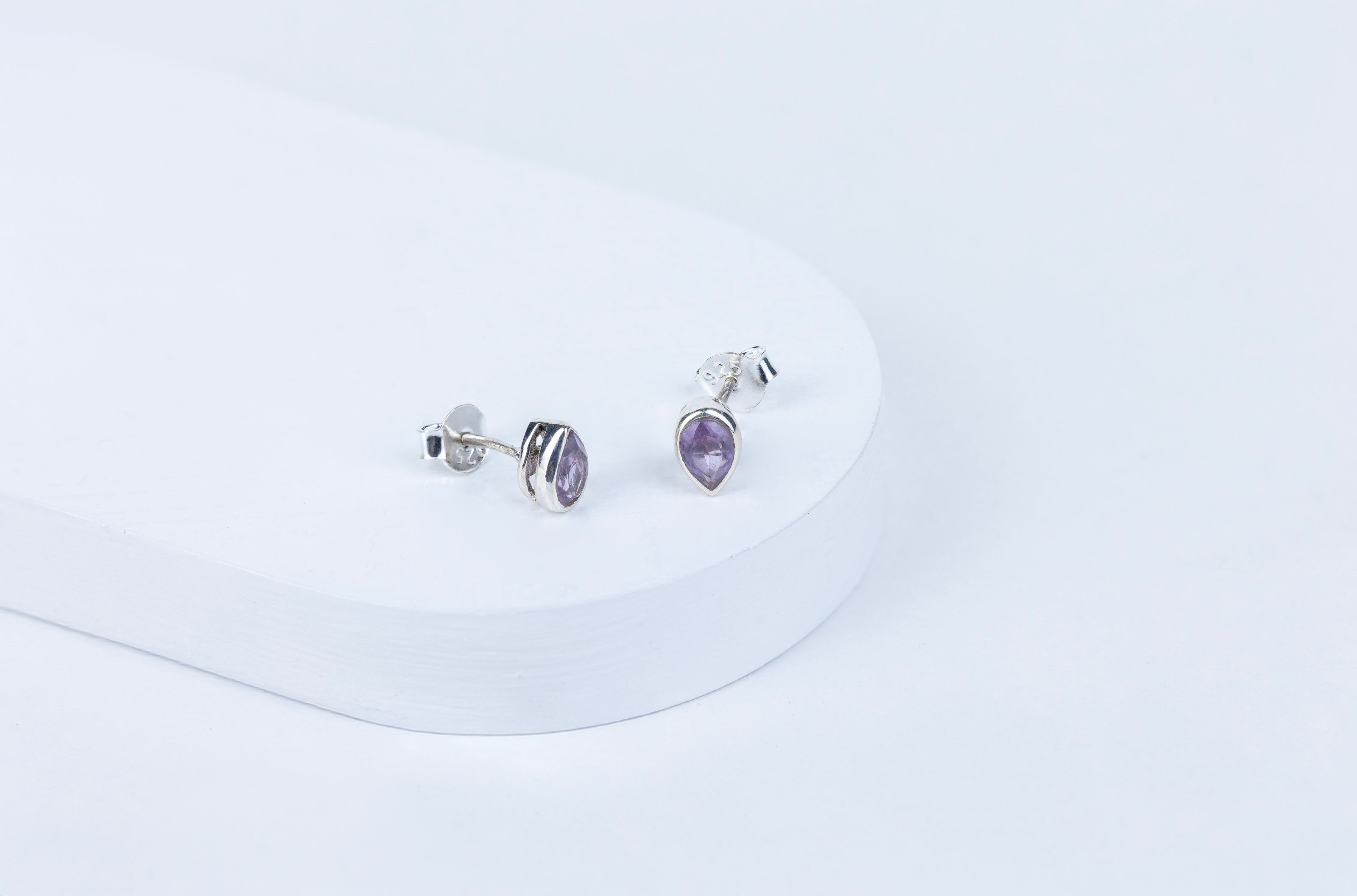 Pair of silver earrings with purple gemstones on a white background