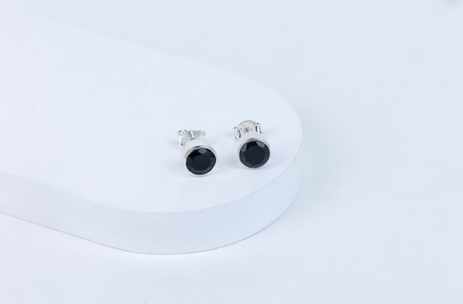 A pair of black tourmaline round earrings displayed on a white stand.