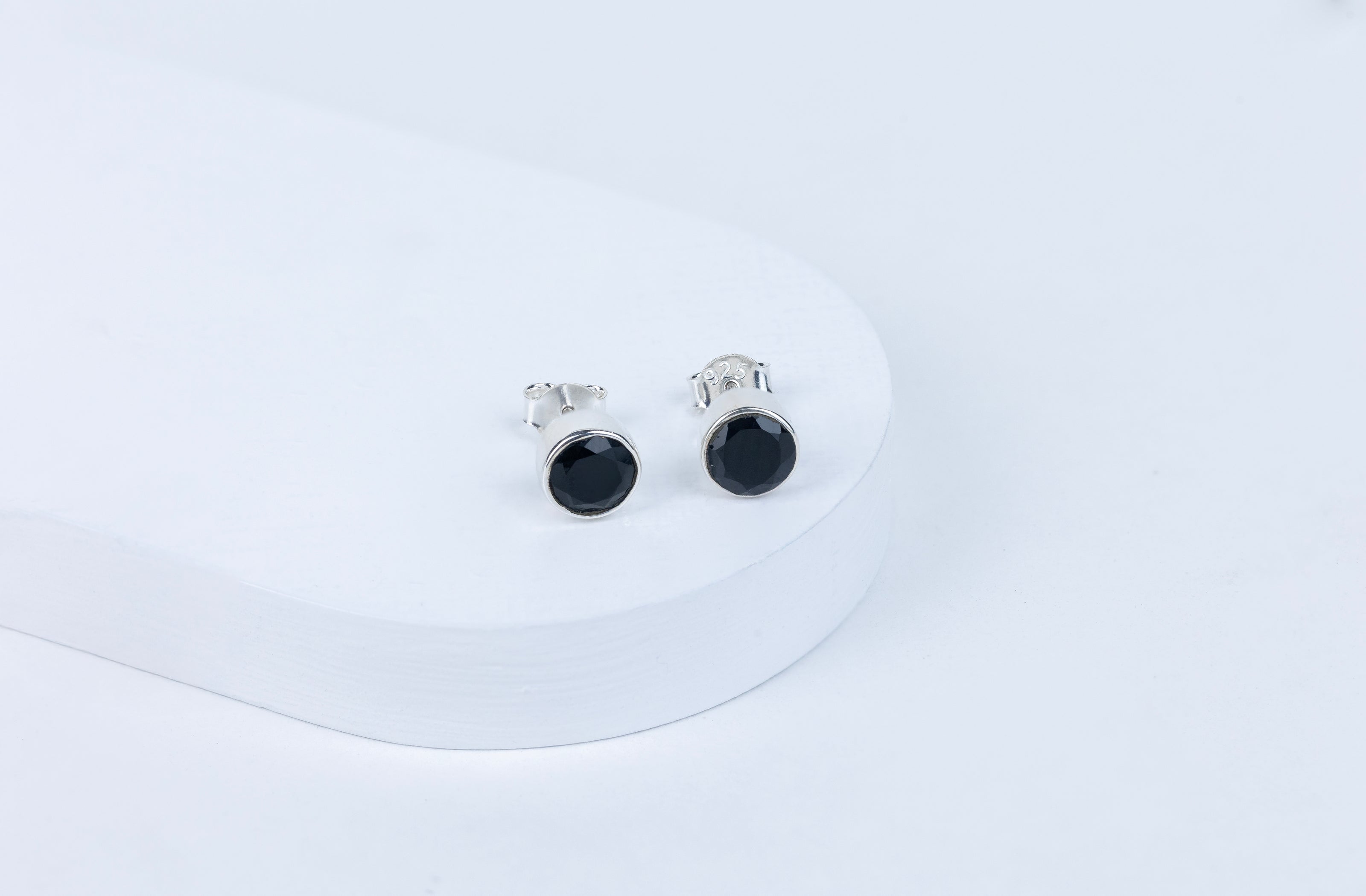 A pair of black tourmaline round earrings displayed on a white stand.