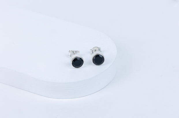 A pair of black tourmaline round earrings displayed on a white stand.