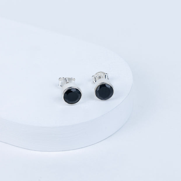 A pair of black tourmaline round earrings displayed on a white stand.