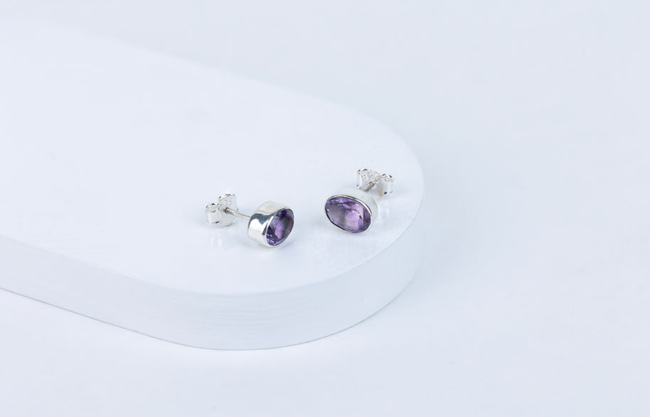 A pair of purple amethyst stud earrings with a faceted cut, displayed against a white background.