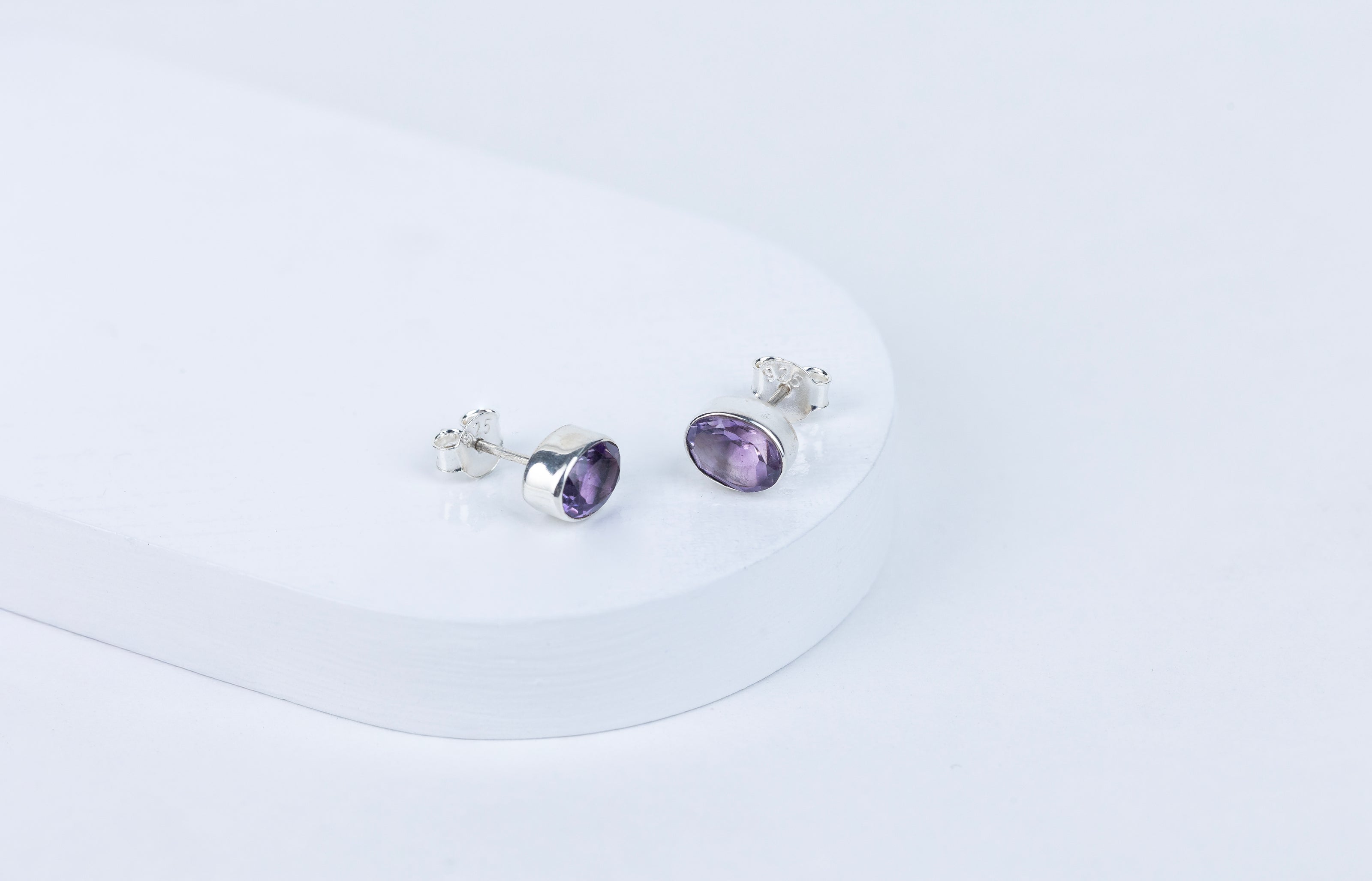 A pair of purple amethyst stud earrings with a faceted cut, displayed against a white background.