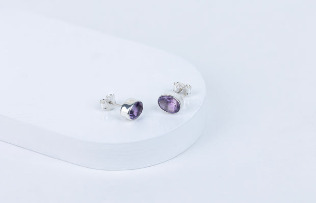 A pair of purple amethyst stud earrings with a faceted cut, displayed against a white background.