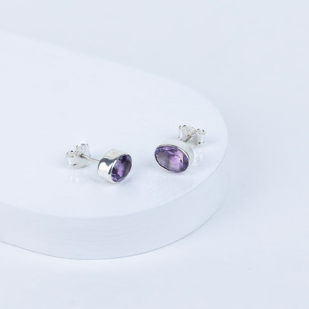 A pair of purple amethyst stud earrings with a faceted cut, displayed against a white background.