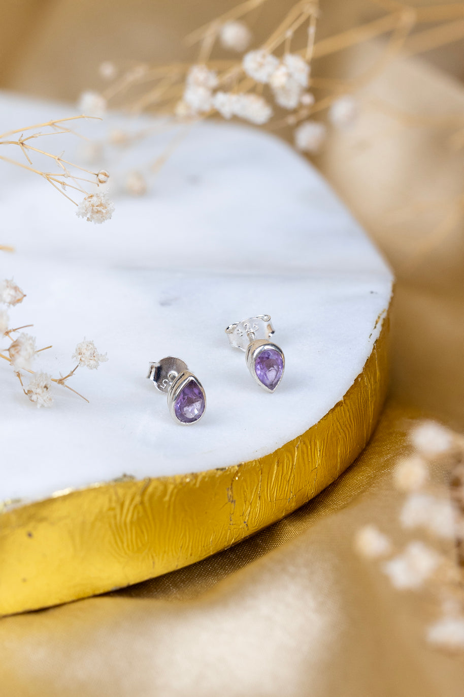 Pair of silver earrings with purple gemstones on a white and gold surface with delicate flowers.