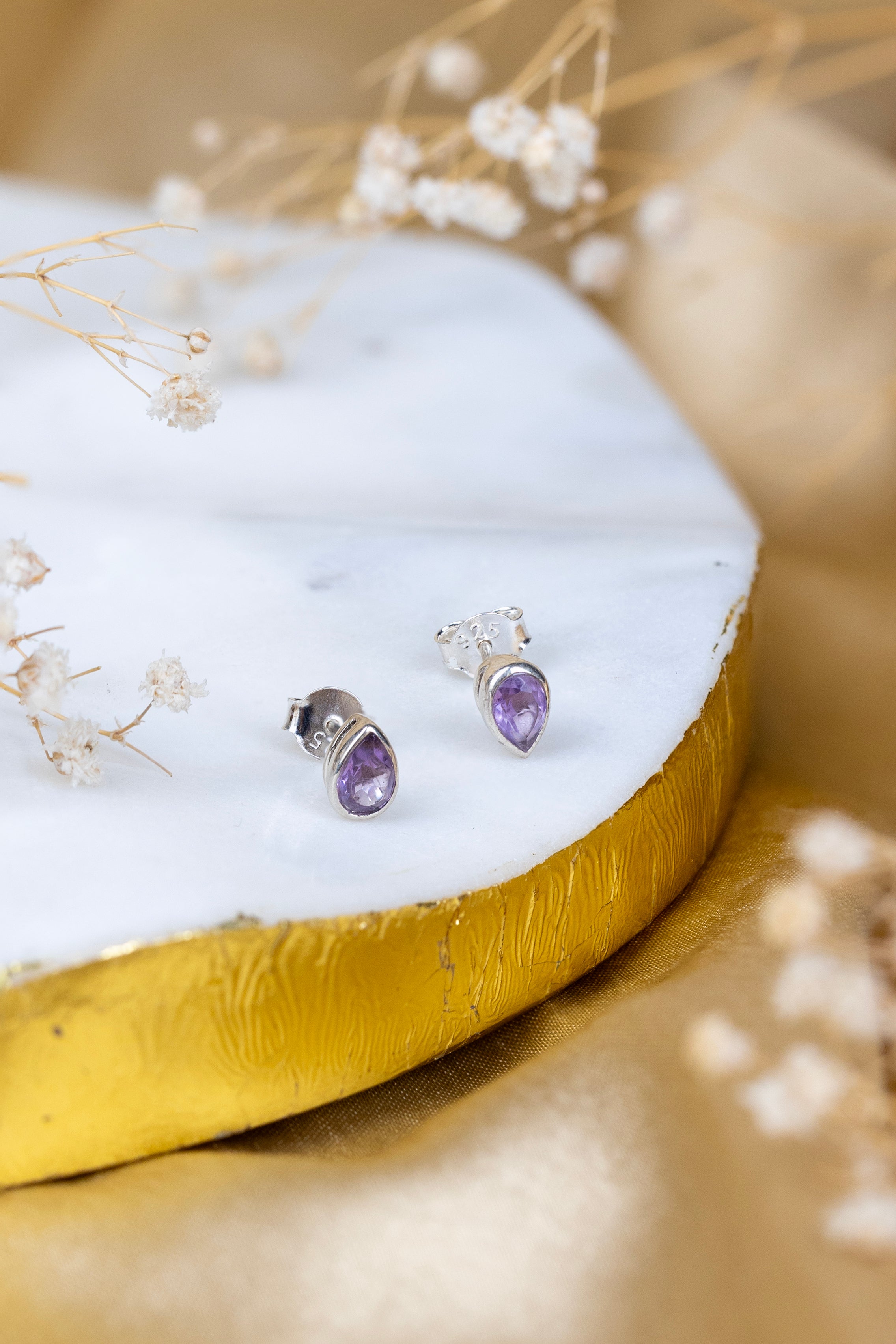 Pair of silver earrings with purple gemstones on a white and gold surface with delicate flowers.