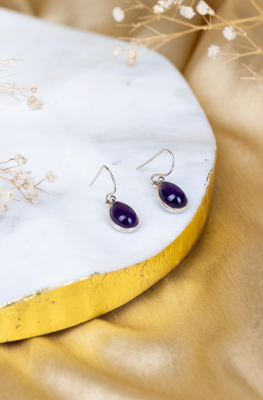 Purple teardrop earrings on a white stand with gold base